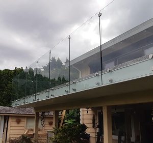 A deck with light blue fascia and a frameless glass railing supported but stainless steel standoffs.