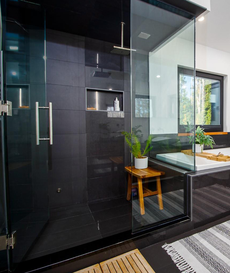 a luxury bathroom with a black tiled shower and glass shower enclosure with a glass pivot door entry